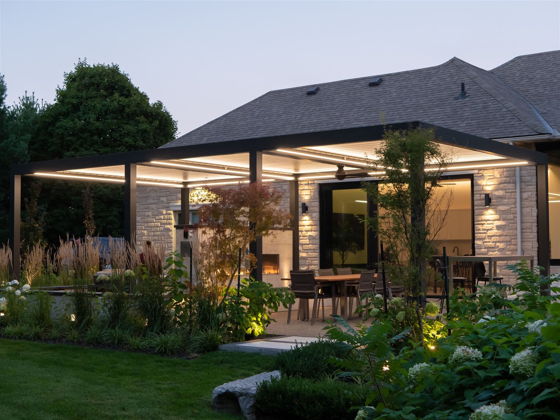 Attached LOUSOL pergola with LED lighting at dusk on a stone house
