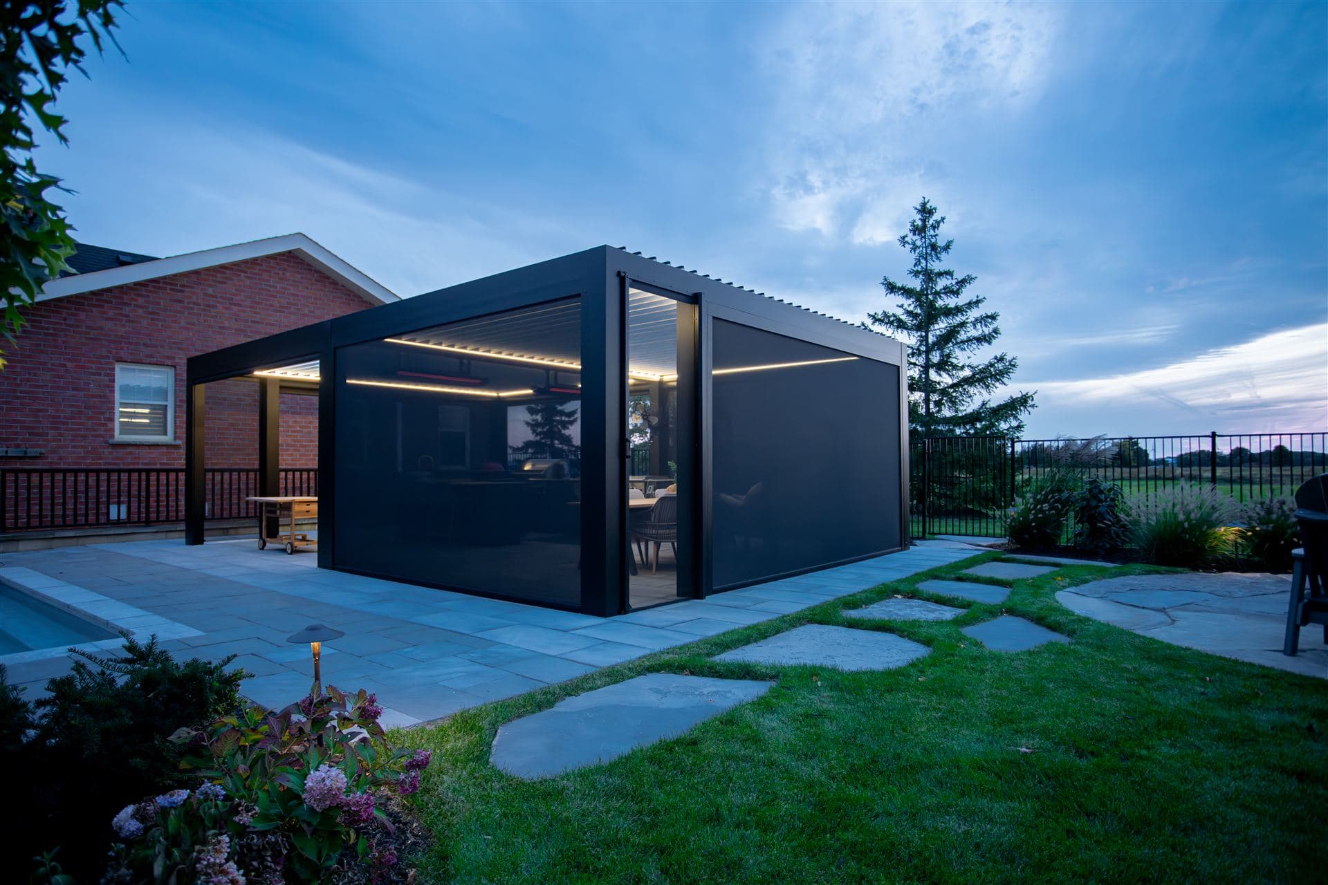 LOUSOL pergola enclosed with zip screens at dusk, LED lighting and heaters inside